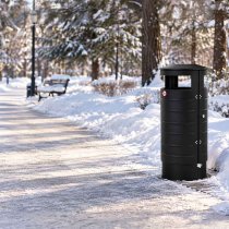 Papperskorg Classic 100L i svart placerad utomhus i en snötäckt park med träd och vintermiljö.